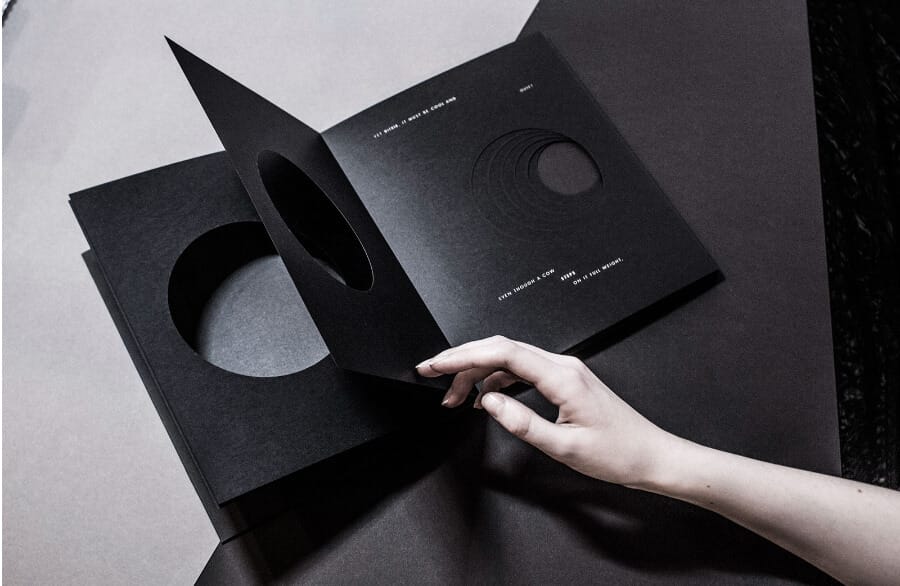 A person opening a book with black pages containing cut-out round shapes, with white text printed on them
